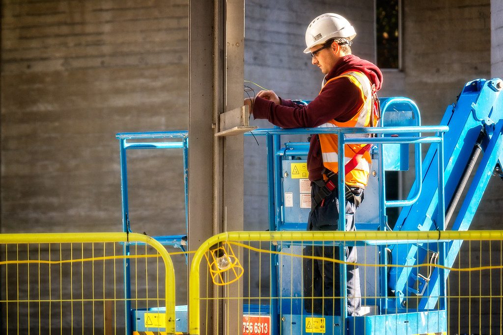 Elektryk na podnośniku przy okablowaniu w obiekcie przemysłowym